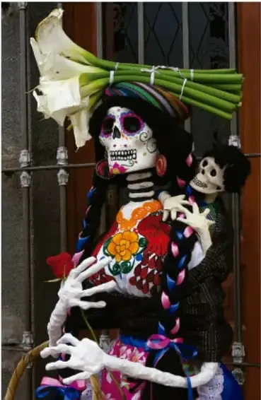 Figura de La Catrina con vestimenta colorida y flores, representación de la muerte en el arte popular mexicano.