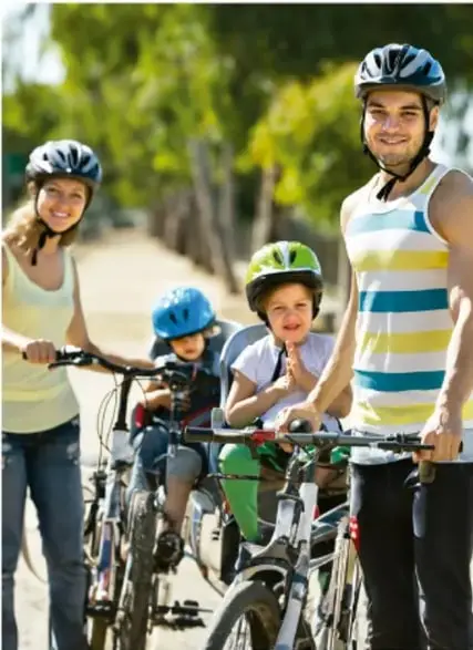 Familia con niños usando cascos y montando bicicletas en una calle arbolada, ejemplo de hábitos saludables y prevención de accidentes.