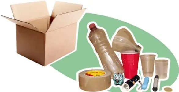Fotografía de materiales del proyecto: caja de cartón abierta, botellas de plástico, vasos, cinta adhesiva y objetos pequeños sobre un óvalo verde.