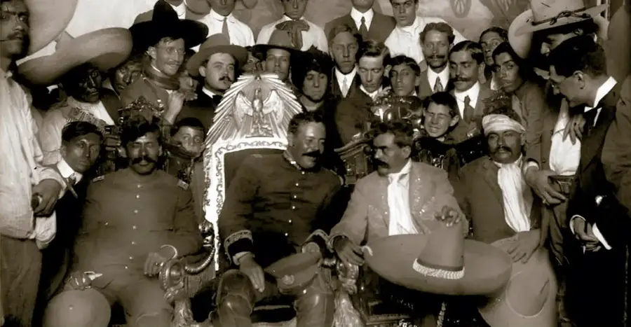 Fotografía histórica del Archivo Casasola: Francisco Villa sentado en la silla presidencial, rodeado de otros revolucionarios y militares. Pie de foto: 'Villa en la silla presidencial. 6 de diciembre de 1914.'