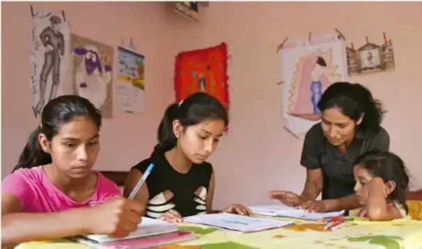 Fotografía de una familia sentada a la mesa trabajando con hojas y lápices, con dibujos y carteles en la pared.