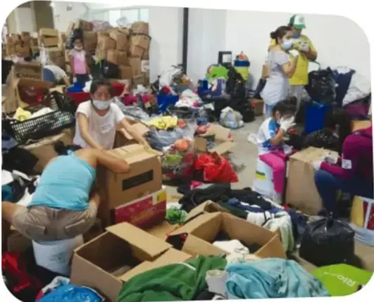 Fotografía de personas, incluidos niños, clasificando y empaquando ropa y víveres en cajas, en un centro de acopio de donaciones.