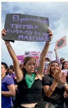Manos entrelazadas con cintas moradas y símbolos de Venus pintados en los nudillos, símbolo del movimiento feminista.
