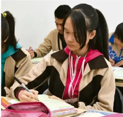 Estudiantes trabajando en equipo con uniformes escolares, escribiendo en sus cuadernos para planear la exposición.