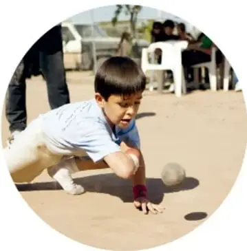 Fotografía de un niño agachado lanzando o golpeando una bola pequeña con el antebrazo, en la modalidad de brazo.