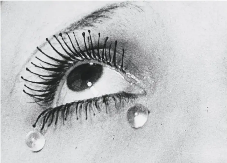 Fotografía en blanco y negro de un ojo humano con pestañas largas y gotas brillantes, que sugiere lágrimas o cristales.