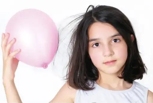 Fotografía de una niña sosteniendo un globo inflado cerca de su cabello, que se levanta por atracción electrostática.
