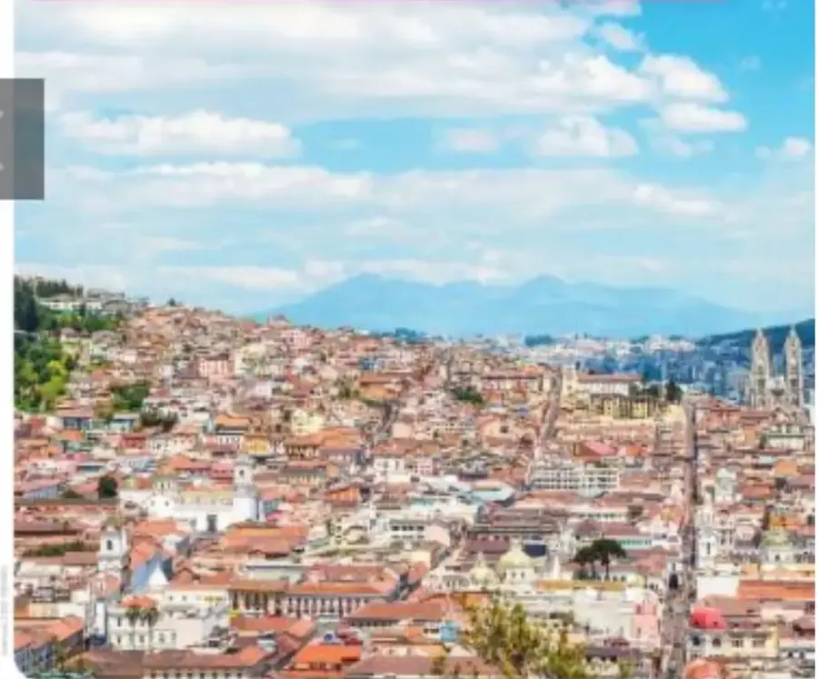 Fotografía panorámica de la ciudad de Quito, Ecuador, con numerosas viviendas, edificios, iglesias, áreas urbanas y montañas al fondo.