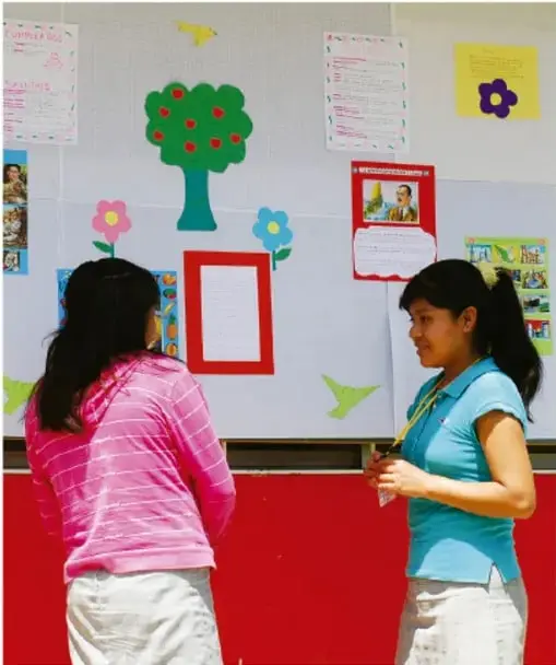 Fotografía de dos estudiantes frente a un periódico mural decorado con árbol, flores y cartel de “Bienvenidos”; crédito: Jesús Eduardo Arteaga Flores, Tamaulipas.