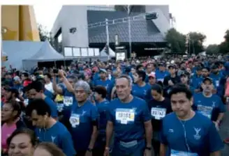 Grupo numeroso de personas con camisetas azules participando en una caminata o evento comunitario de actividad física.