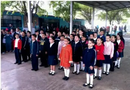 Grupo de estudiantes de primaria formados en el patio de la escuela, con uniforme.
