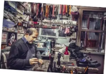 Fotografía de un artesano trabajando en su taller rodeado de herramientas y objetos colgados, como ejemplo de oficio y saber comunitario que puede exponerse.
