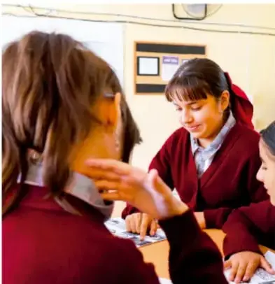 Fotografía de estudiantes de telesecundaria con uniforme chamarra roja trabajando colaborativamente alrededor de una mesa.