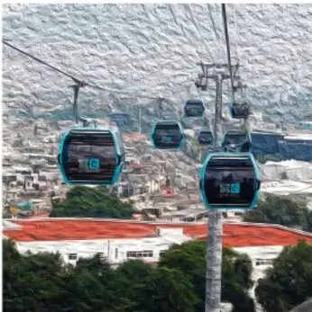 Fotografía de un teleférico que cruza sobre una ciudad, con montañas al fondo y edificios con techos rojos.