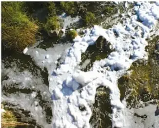 Fotografía aérea de un río o arroyo de agua cristalina que corre entre rocas y vegetación verde.