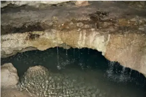 Interior del Cuexcomate: pozo con agua oscura rodeado de paredes rocosas húmedas.