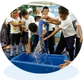 Foto circular de niños recibiendo agua de una llave sobre un contenedor azul.
