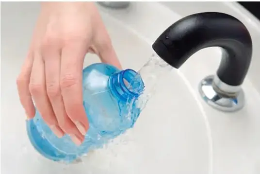 Fotografía de una mano sosteniendo e inclinando una botella plástica azul bajo un grifo, mientras sale agua y se forman burbujas.