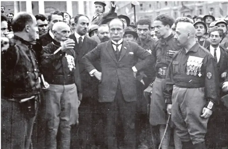 Fotografía en blanco y negro de Benito Mussolini junto a otros dirigentes fascistas en una concentración pública.