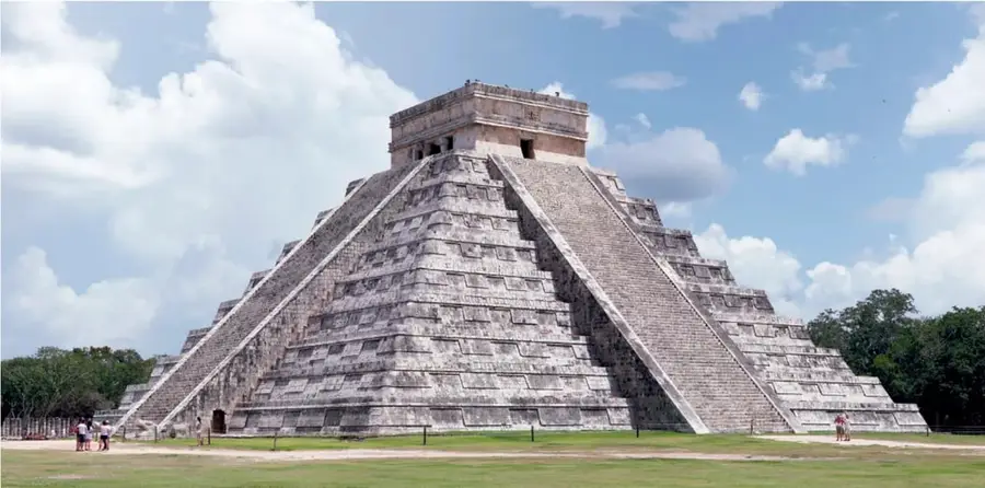 Pirámide escalonada de base cuadrada con escalinata central y templo en la cima, bajo cielo con nubes; al pie, visitantes y vegetación. Corresponde al Castillo de Kukulcán, Chichén Itzá.